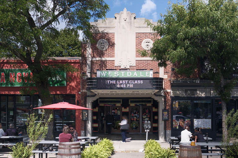 Exterior view of the Westdale Theatre, displaying its new marquee and its integration with neighbouring storefronts, including a pizza place and a restaurant with outdoor seating.